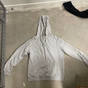 Ljusgrå hoodie i ekologisk bomull - Säljer en ljusgrå hoodie från C i ekologisk bomull. Tröjan har huva med dragsko och en stor magficka framtill. Perfekt för en avslappnad stil och enkel att matcha med det mesta.