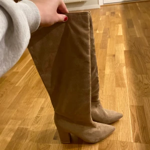 Beiga höga stövlar med klack - Säljer ett par snygga beiga stövlar med hög klack! Köpta från Nelly strl 39 kan användas både vinter ocu sommar passar bra till en snygg klänning eller en snygg höstoutfit! Aldrig använd utomhus endast testar dom inne 