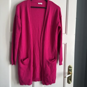 Ceriserosa stickad kofta från Name It - Säljer en ceriserosa stickad kofta från Name It. Koftan har långa ärmar, två fickor framtill och en öppen design utan knappar. Perfekt för lager-på-lager och enkel att matcha med olika outfits.