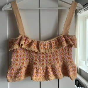 Beige stickad croppad linnetopp med volang - Supersöt beige croppad stickad linnetopp med breda axelband och volangdetaljer. Toppen har ett mönster i rosa, orange och gul och är perfekt för varma dagar. Har använt en gång så säljer. Skicka för fler frågor💛