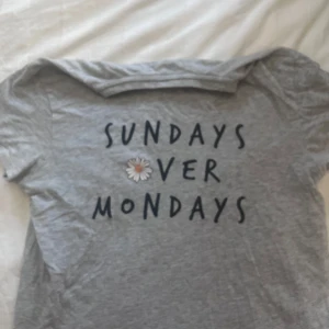Grå t-shirt med tryck från Primark - Grå t-shirt från Primark med texten 'Sundays over Mondays' och en liten blomdetalj i mitten. T-shirten har rund halsringning och korta ärmar. Perfekt för en avslappnad stil.