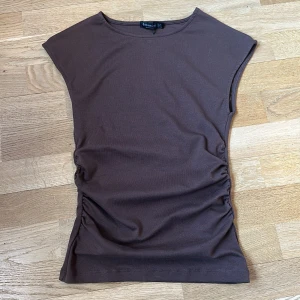 Brun topp från Stradivarius - Säljer en brun topp från Stradivarius i mjuk bomull. Toppen har ärmlös design och rynkade sidor som ger en snygg detalj. Perfekt att styla med jeans eller kjol för en trendig look.