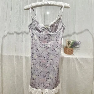 Blommig spetsklänning med pastellfärger - Söt kort klänning med blommigt mönster i pastellfärger. Klänningen har tunna axelband, spetsdetaljer vid byst och nederkant samt en liten rosett framtill. 