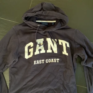 Mörkblå hoodie från GANT - Säljer en mörkblå hoodie från Gant. Klassisk huva med dragsko och mjukt material. Perfekt för en avslappnad stil.