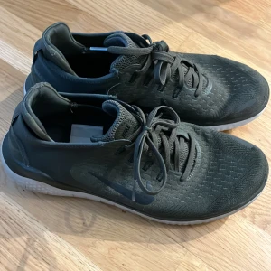 Svarta Nike sneakers med snörning - Säljer ett par svarta Nike sneakers med diskret logga på sidan. Skorna har snörning, rund tå och ovandel i textil med mönstrad struktur. Sulan är vit och har ett unikt mönster undertill. Perfekta för vardagsbruk eller träning.