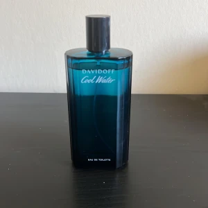 Davidoff Cool Water Eau de Toilette - Davidoff Cool Water Eau de Toilette med en stilren, djupblå glasflaska och svart lock. Doften är fräsch och klassisk, perfekt för dig som gillar marina och friska toner. Flaskan rymmer 125 ml och har en modern, kantig design. parfymen använda en gnutta och pris diskuteras.