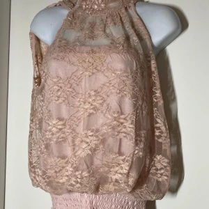 Ljusrosa spetsblus från Sisters Point - Säljer en ljusrosa blus från Sisters Point i transparent spets med blommönster. Toppen är ärmlös och har hög hals samt smockad nederkant. Perfekt för dig som gillar romantisk stil och fina detaljer.