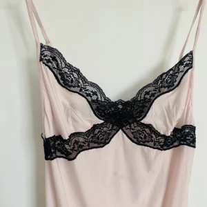 Ljusrosa slipklänning med svarta spetsdetaljer - Säljer ett ljusrosa nattlinne med tunna axelband och  svarta spets detaljer. Har en liten fläck som syns på sista bilden🩷