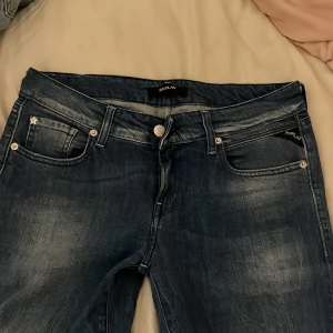 Replay jeans i blå denim - Snygga blå jeans från Replay med klassisk femficksdesign och diskreta slitningar. Byxorna har raka ben och silverfärgade nitar samt knappar. Bakfickorna har dekorativa nitar i mönster. Perfekta för en avslappnad stil.