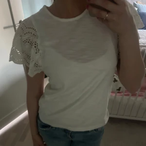 Vit topp med spetsärmar - Säljer en söt vit topp med korta ärmar i spets och rund halsringning. Perfekt för dig som gillar romantiska detaljer och enkel stil. Toppen är i mjukt material och passar till både jeans och kjol.