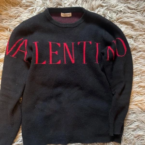 Valentino tröja - Säljer en svart stickad tröja från Valentino med stor röd logotyp över bröstet. Tröjan har rund halsringning och långa ärmar. Perfekt för dig som gillar exklusiva och stilrena plagg med en statement-detalj. Passar M men även S. Passar perfekt nu när de är varmare väder så behöver man ingen jacka. Bara att höra av sig vid minsta fundering! Priset är ej hugget i sten🪨📦