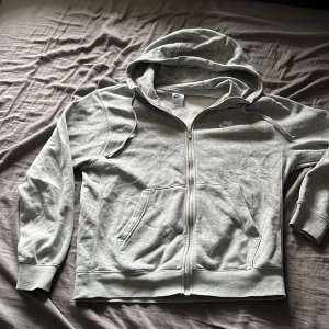 Ljusgrå hoodie med dragkedja från Nike - Säljer en ljusgrå hoodie från Nike i storlek M. Tröjan har dragkedja framtill, huva och två fickor. Mjuk insida och klassisk Nike-logga på bröstet. Perfekt för en avslappnad stil. Bra skick använd fåtal gånger