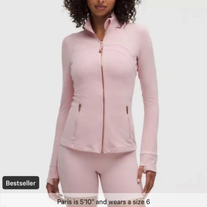 Ljusrosa träningsjacka med dragkedja - Snygg ljusrosa träningsjacka med hel dragkedja framtill. Jackan har långa ärmar och två fickor med dragkedja. Figurnära passform som passar perfekt till träning. Från lullulemon i storlek 2
