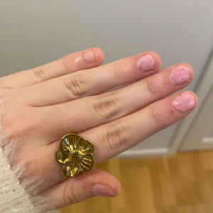 Guldfärgad blomring - Säljer en snygg guldfärgad ring i form av en blomma. Ringen har en blank yta och är ett riktigt statement-smycke som drar blickarna till sig. Perfekt för dig som vill ha något unikt och trendigt!