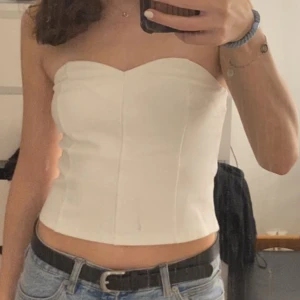Tubtopp  - Säljer en stilren vit tubtopp med hjärtformad urringning. Toppen har en smockad detalj baktill för extra komfort. Perfekt att matcha med jeans eller kjol för en trendig look.
