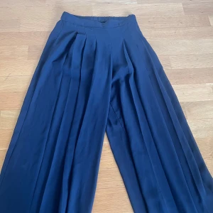 Vida svarta byxor från Bik Bok - Säljer ett par svarta vida byxor från Bik Bok i storlek 34. Byxorna har hög midja, veck framtill och är tillverkade i ett tunt, flowy material som ger en snygg siluett. Perfekta för dig som gillar en loose och bekväm stil.