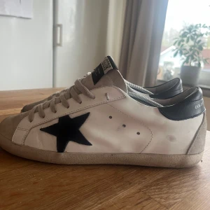 Golden Goose sneakers - Golden Goose sneakers i vitt skinn med mörkblå stjärna. Storlek 42.5 har själv 43 och passar perfekt. Kvalitenr bra förutom att sulan har börjat gå upp lite. Dustbag ingår. Priset kan diskuteras.