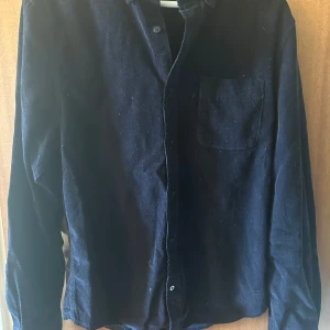 Mörk blå manchesterskjorta från Dressmann - Säljer en mörk blå långärmad skjorta i manchester från Dressmann. Skjortan har klassisk krage, bröstficka och knäppning framtill. Perfekt för dig som gillar en stilren och tidlös look.