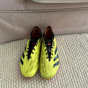 Gula Adidas Predator fotbollsskor med påse  - Säljer ett par gula Adidas Predator fotbollsskor med svarta detaljer och röda dobbar. Skorna har snörning. Perfekta för dig som vill sticka ut på planen!