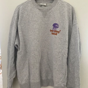 Grå sweatshirt från H&M med tryck - Grå sweatshirt från H&M med trycket 'low-key land' i brunt och lila motiv av svamp, blomma och snigel både fram och bak. Mjuk bomullskänsla och ribbade muddar vid ärmslut och nederkant. Perfekt för en avslappnad stil.