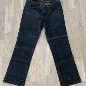Svarta jeans från Cue Denim - Säljer ett par svarta jeans från Cue Denim i storlek 42. De har en klassisk femficksdesign med orange sömmar som ger en snygg kontrast. Jeansen har en knapp och dragkedja framtill. 