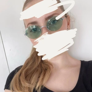 Runda solglasögon med gröna linser - Säljer ett par coola runda solglasögon med gröna linser. De har en tunn metallbåge som ger en minimalistisk look. Perfekta för en solig dag och ger en retro vibe. Passar både till vardags och fest!