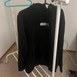 Svart hoodie från Hoodrich - Säljer en svart hoodie från Hoodrich i storlek medium. Den är superbekväm och perfekt för både chill och vardagsbruk. Hoodien har en klassisk design med en känguruficka och justerbar dragsko i huvan. Texten 'Hoodrich' är tryckt på bröstet. Perfekt för höst och vinter!