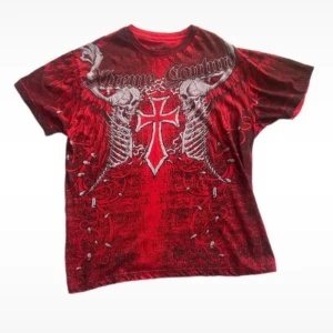 Röd t-shirt från Xtreme Couture - Säljer en cool röd t-shirt från Xtreme Couture med ett grymt tryck av vingar och kors på både fram- och baksidan. T-shirten är i storlek Large och är perfekt för dig som vill sticka ut. Den är gjord av bomull och har korta ärmar. Perfekt för en avslappnad stil eller för att rocka på en fest!