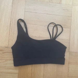 Svart sport-bh med dubbla axelband - Säljer en svart sport-bh från G i storlek S. Den har dubbla axelband på ena sidan och enkel på andra, vilket ger en cool asymmetrisk look. Perfekt för träning eller vardagsbruk. Materialet är stretchigt och bekvämt.