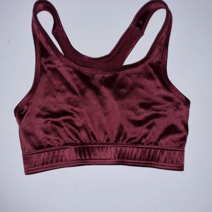 Vinröd sport-bh från Newbody - Säljer en snygg och bekväm vinröd sport-bh från Newbody. Den är tillverkad i ett glansigt material som känns mjukt mot huden. Perfekt för träning eller vardagsbruk. Den har en tight passform och breda axelband för extra stöd.
