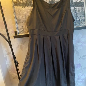 Svart klänning med veckad kjol - Elegant svart klänning med veckad kjol och breda axelband. Perfekt för en stilren look. Klänningen har en klassisk design som passar många tillfällen.