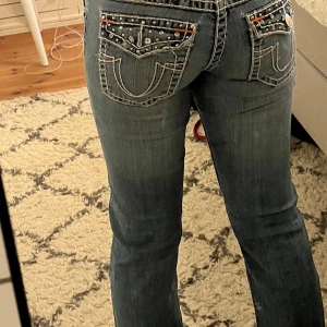 Bootcut jeans med coola detaljer - Snygga blå jeans med unika detaljer som broderade bakfickor och nitar. De har en bootcut-stil och låg midja, jag är 168 för referens✨ är lite slitna längst ner på ett av benen men inget som märks av.