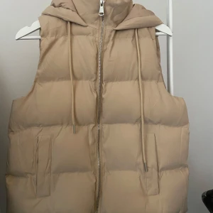 Beige dunväst med huva från Chelsea - Beige väst från Chelsea med dragkedja och huva. Använd endast några fåtal gånger dvs väldigt bra skick. Nypris 600kr men jag säljer den för 120. Har du frågor är det bara att höra av dig🧡