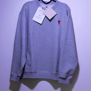 Ami Paris Sweatshirt - Helt ny Ami Paris sweatshirt med ett rött A-hjärta broderad märke på bröstet. Tröjan har en klassisk rund halsringning. Perfekt för en snygg stil.