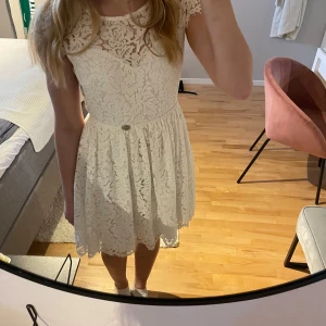 Vit spetsklänning med öppen rygg - Söt vit spetsklänning med korta ärmar och en elegant öppen rygg. Klänningen har en rund halsringning och ett fint spetsmönster över hela tyget. Perfekt till student eller konfirmation! Endast använd 1 gång. 