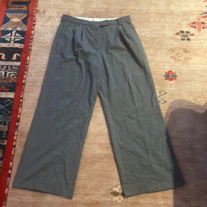 Grå vida byxor - Säljer ett par grå byxor med vid passform. Byxorna har en klassisk design med knappar och dragkedja i midjan. Perfekta för en stilren look.