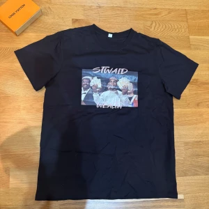 Svart t-shirt med tryck - Snygg svart t-shirt med ett coolt tryck av personer som håller i pengar och texten 'STWAID WEALTH'.