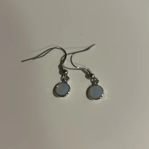 Silverörhängen med ljusblå sten - Snygga silverörhängen med en rund ljusblå sten. Perfekta för att ge en elegant touch till din outfit. De har en enkel krok för enkel användning.Tvättar innan skickar.