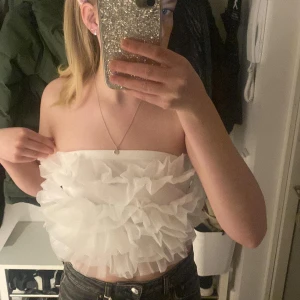 Vit axelbandslös topp med volanger - Säljer en söt vit axelbandslös topp med volanger. Perfekt för sommarens fester. Toppen är croppad och har en luftig design.