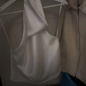 Vit satinlinne från Zara - Säljer ett elegant vitt satinlinne från Zara. Toppen har en draperad design och öppen rygg vilket blir en stilren look. Perfekt för en kväll ute eller en speciell tillställning.