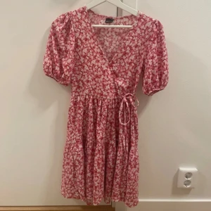 Omlottklänning  - Blommig omlottklänning i rosa och rött från Gina Tricot. Använd fåtal gånger och i superfint skick! 