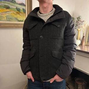 Grå jacka från Moncler - Säljer en snygg grå jacka från Moncler med svarta puffer ärmar. Jackan har en stilren design med knappar och dragkedja framtill samt praktiska fickor. Perfekt för kyligare dagar. Den har en lagad dragkedja som funkar strålande. Vid ytterligare frågor skicka DM! 