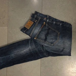Mörkblå jeans från Nudie Jeans - Säljer ett par snygga mörkblå jeans från Nudie Jeans. De har en klassisk femficksdesign och orangea sömmar som ger en cool kontrast. Perfekta för en avslappnad stil. 9/10 skick