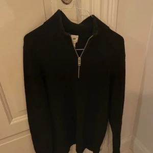 Svart tröja med dragkedja från H&M - Säljer en stilren svart tröja från H&M med dragkedja i halsen. Perfekt för kyligare dagar och enkel att matcha med olika outfits. Tröjan har långa ärmar och är tillverkad i ett mjukt material.