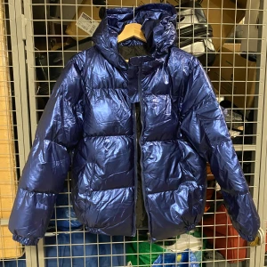 Blå glansig pufferjacka - Snygg blå pufferjacka med glansigt material och dragkedja framtill. Jackan har en hög krage och långa ärmar, perfekt för kyliga dagar. Den har en modern look och är både stilren och funktionell.