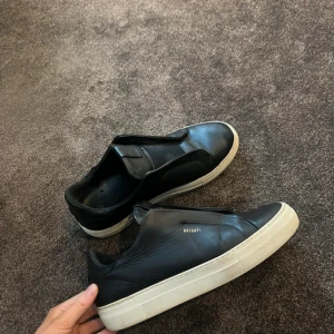 Axel Arigato Laceless Sneakers - Snygga svarta sneakers från Axel Arigato med vit sula. Skorna har en stilren design utan snörning och är perfekta för en minimalistisk look.