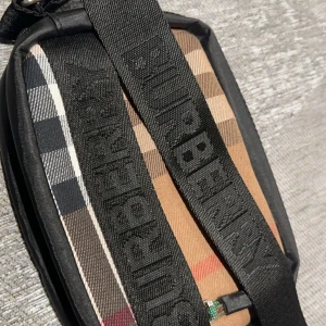 Rutig axelväska från Burberry - Snygg rutig axelväska från Burberry med klassiskt mönster i beige, svart och rött. Väskan har en justerbar axelrem med logotyp och en dragkedja framtill. Perfekt för att bära dina nödvändigheter med stil. Har aldrig andvänt den och den är i topp skick.
