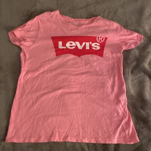 Rosa t-shirt från Levi's - Säljer en rosa t-shirt från Levi's med det klassiska röda och vita logotyptrycket på bröstet. T-shirten är använd fåtals gånger och är i bra skick. 