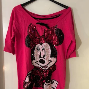 Rosa tröja med paljetter och Disney-motiv - Säljer en rosa tröja med ett stort Disney-motiv av en karaktär i paljetter på framsidan. Tröjan har trekvartsärm och en lös passform. Perfekt för den som älskar färgglada och lekfulla plagg!