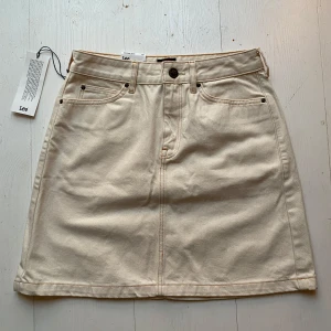 Beige kjol från Lee - Snygg beige kjol från Lee i jeansmaterial. Kjolen har en klassisk femficksdesign med knapp och dragkedja fram. Ny med prislapp